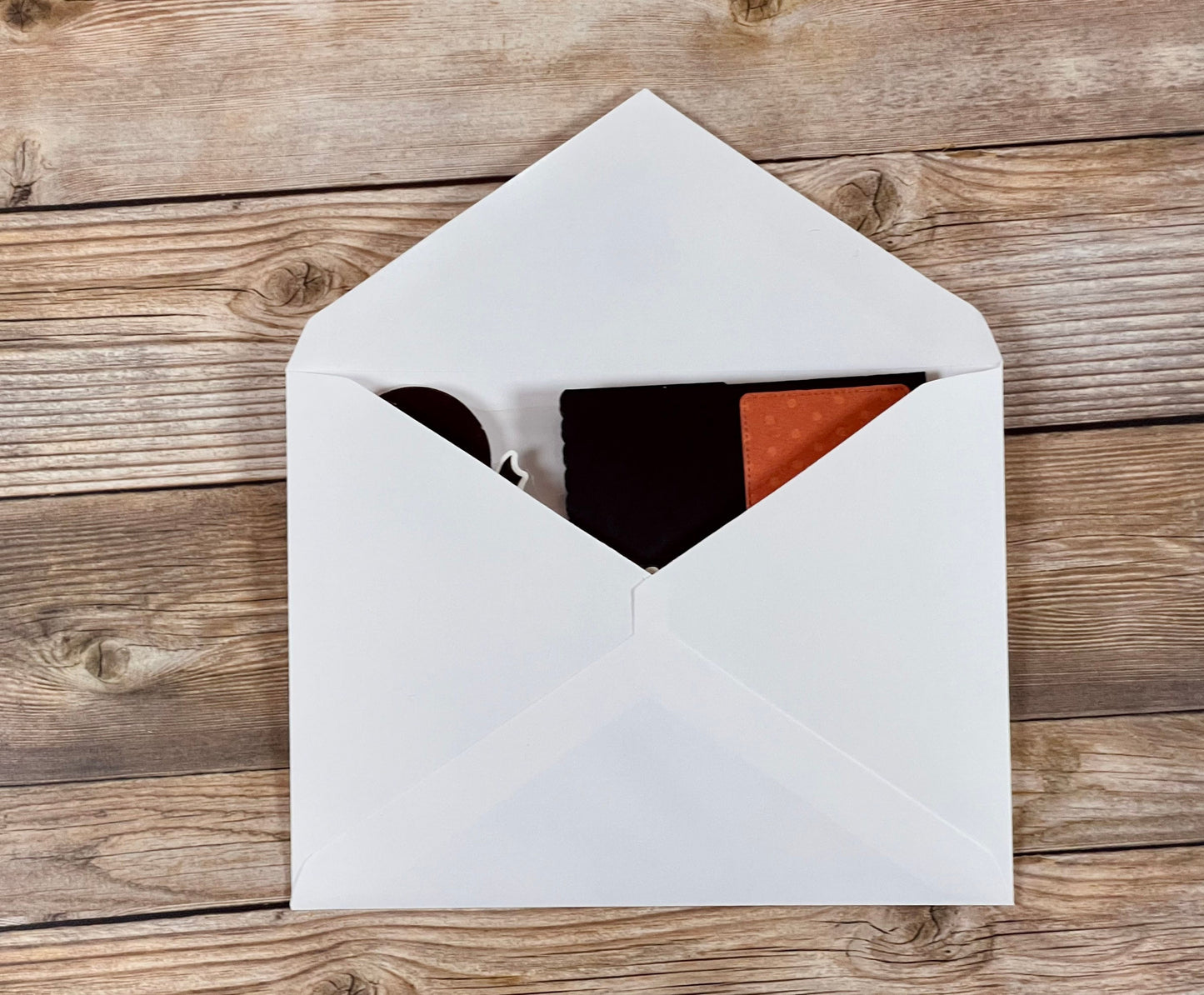 Open white envelope with black and red items on a wooden surface