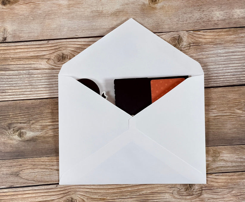 Open white envelope with black and red items on a wooden surface