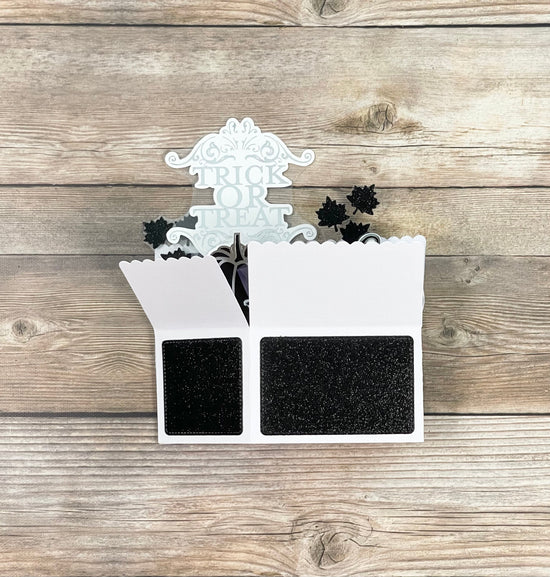 Decorative Halloween pop-up card with black spider webs and a white top on a wooden surface