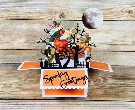 Pop-up Halloween card with trees, moon, and 'Spooky Greetings' text on a wooden surface
