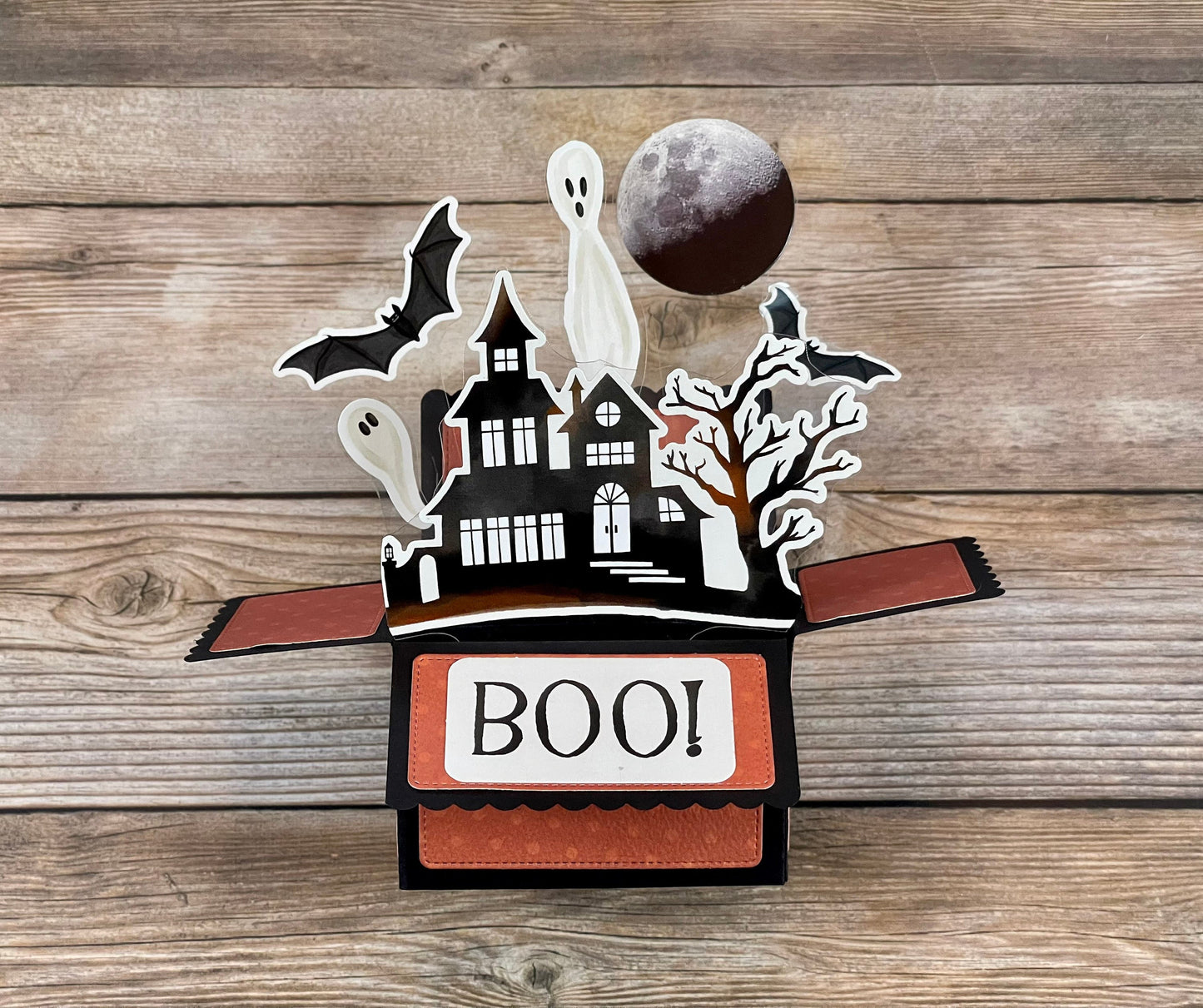 Halloween-themed pop-up box with ghosts, bats, and a moon on a wooden surface
