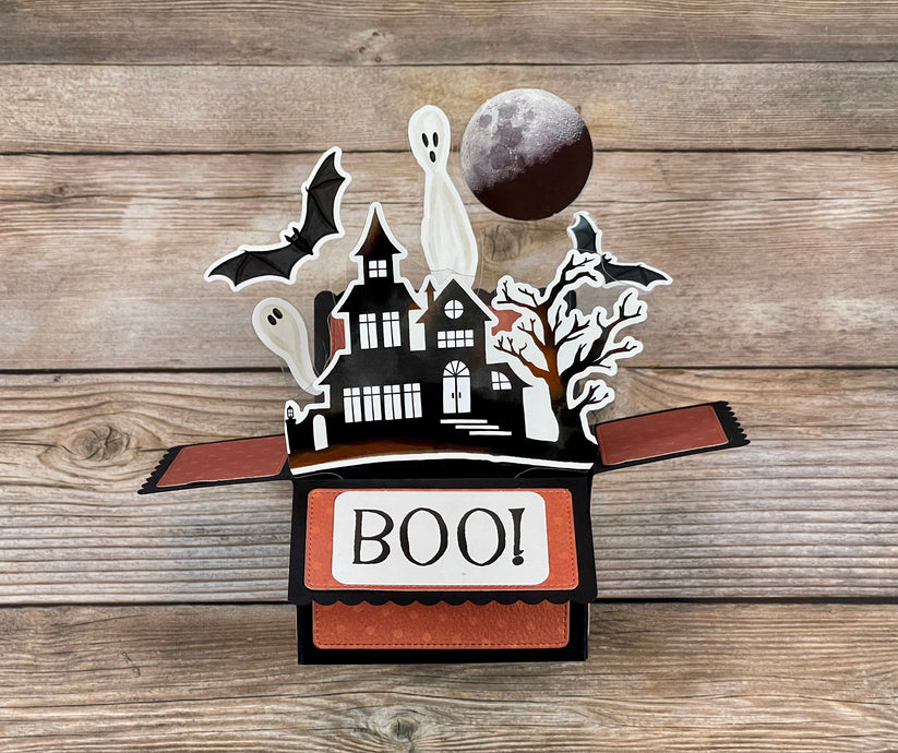 Halloween-themed pop-up box with ghosts, bats, and a moon on a wooden surface