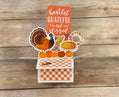 Thanksgiving-themed card with a turkey, pumpkins, pie, and cornucopia on a wooden background.