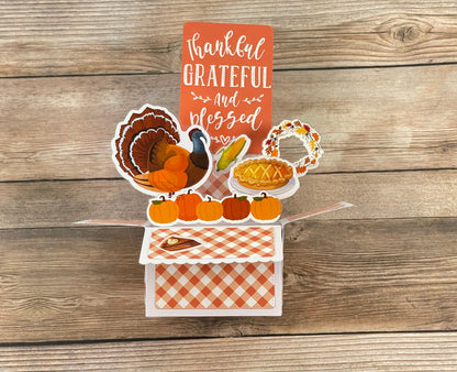 Thanksgiving-themed card with a turkey, pumpkins, pie, and cornucopia on a wooden background.