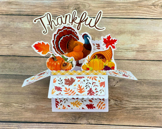 3D box pop-up card with a turkey, pumpkins, and fall leaves on a wooden background