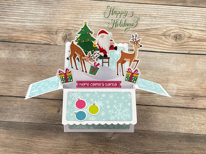 Pop-up Christmas card with Santa Claus and reindeer on a wooden surface
