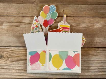 Decorative birthday card with colorful balloons and party elements on a wooden surface