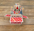 Pop-up birthday card with dog illustration, candles, and 'Happy Birthday' text on a wooden surface.
