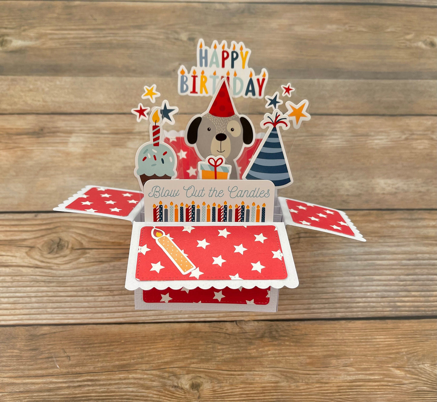 Pop-up birthday card with dog illustration, candles, and 'Happy Birthday' text on a wooden surface.