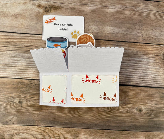 Folded cat-themed pop-up card with 'meow' text on a wooden surface