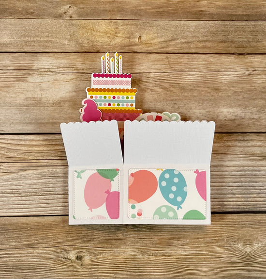 Card with a cake and balloons design on a wooden surface