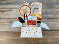 Pop-up birthday card with carnival-themed elements on a wooden surface