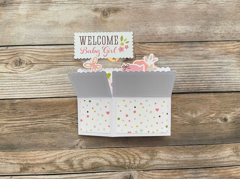 Card with 'Welcome Baby Girl' text on a wooden surface