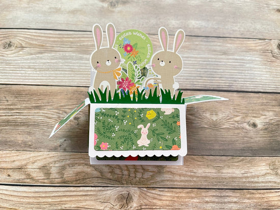 Pop-up card with bunnies and flowers on a wooden surface