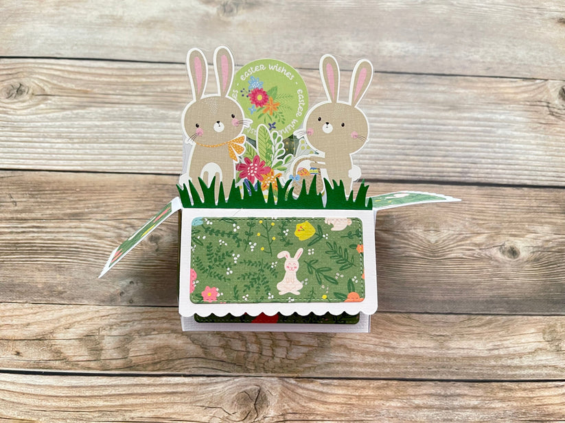 Pop-up card with bunnies and flowers on a wooden surface