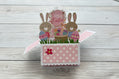 Easter-themed pop-up card with bunnies and an egg on a wooden background