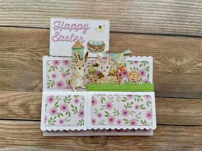 Easter-themed pop-up card with bunnies and flowers on a wooden surface