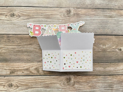 Open card with 'BABY' banner on a wooden surface