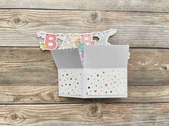 Open card with 'BABY' banner on a wooden surface