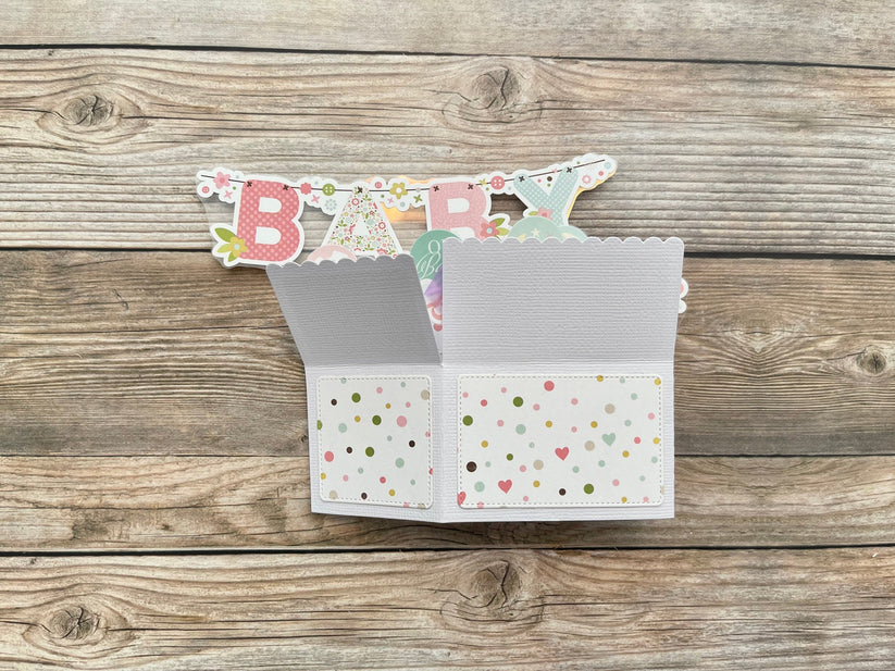 Open card with 'BABY' banner on a wooden surface