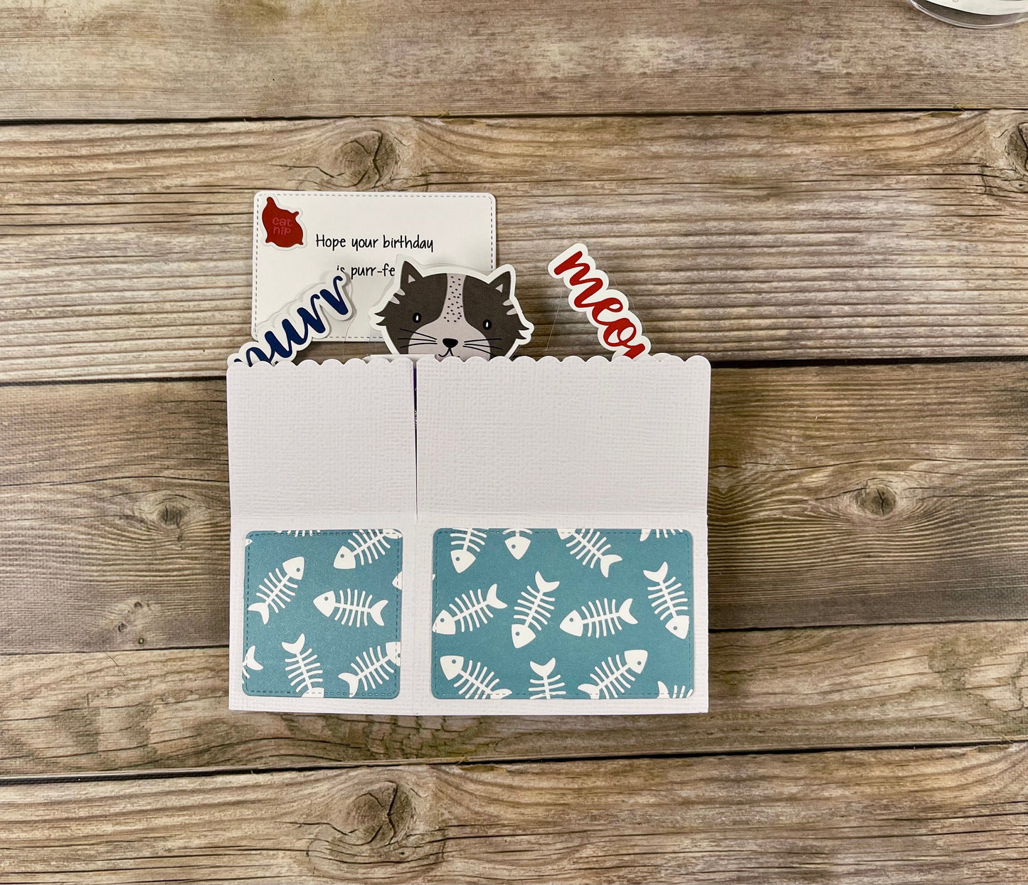 Card with fish pattern and cat-themed cutouts on a wooden surface