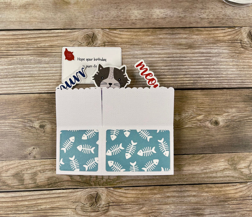 Card with fish pattern and cat-themed cutouts on a wooden surface