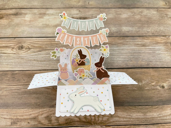 Easter-themed pop-up card with bunnies and eggs on a wooden surface