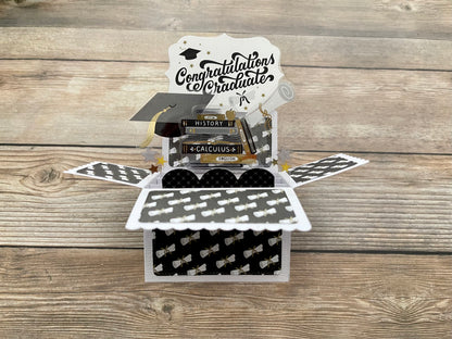 Graduation-themed pop-up card with books and mortarboard on a wooden surface