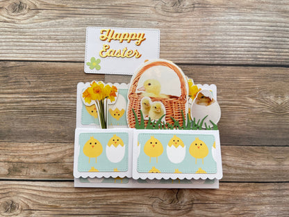 Easter-themed card with chicks, basket, and flowers on a wooden surface