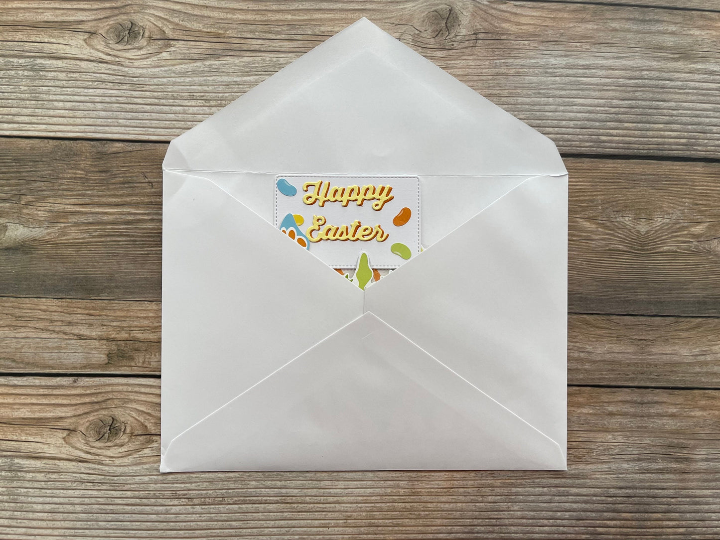 White envelope with a 'Happy Easter' card on a wooden surface