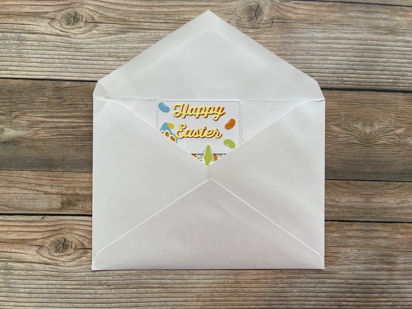 White envelope with a 'Happy Easter' card on a wooden surface