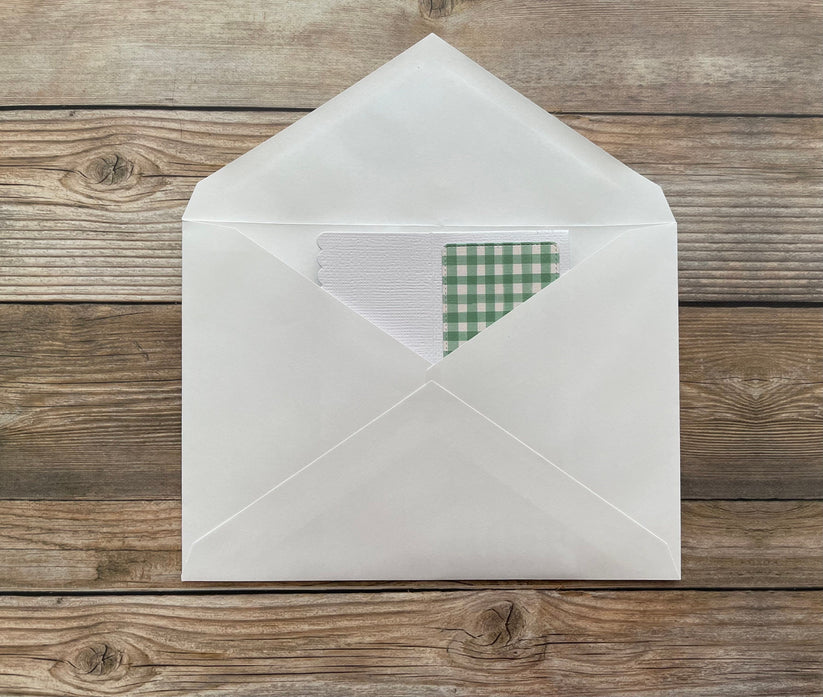 White envelope with a green checkered card on a wooden surface