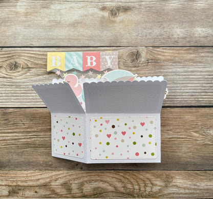 Open card with polka dot design and baby-themed elements on a wooden background