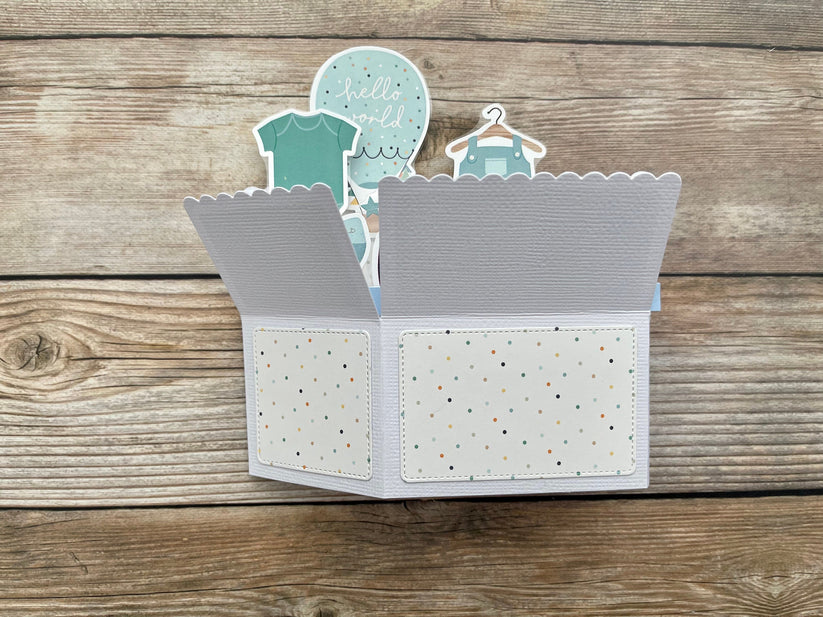 Open card with baby-themed elements on a wooden surface