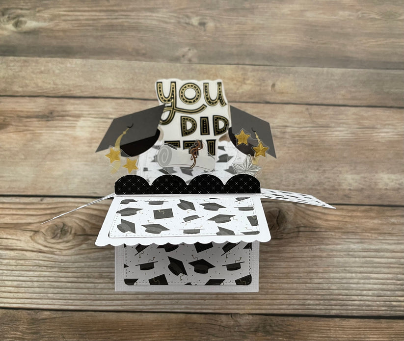 Graduation-themed pop-up card with 'YOU DID IT!' text on a wooden surface