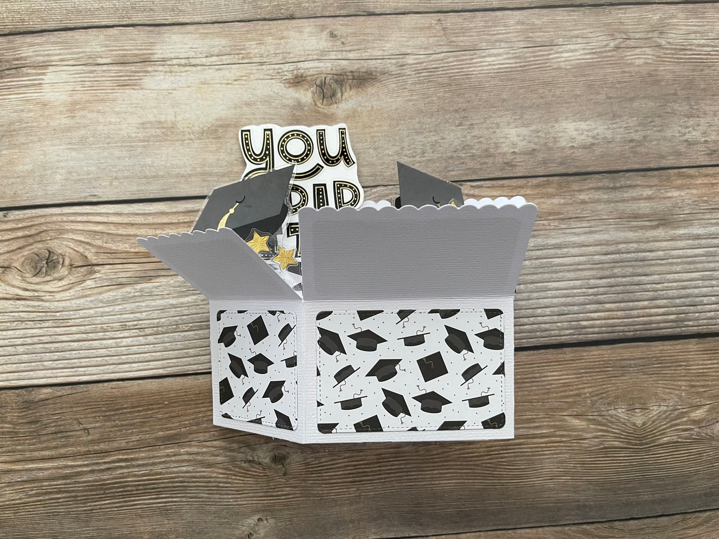 Decorative box with graduation cap pattern and 'You Did It!' topper on a wooden surface