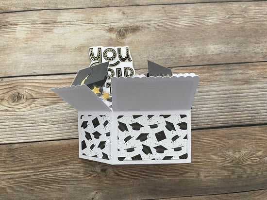 Decorative box with graduation cap pattern and 'You Did It!' topper on a wooden surface