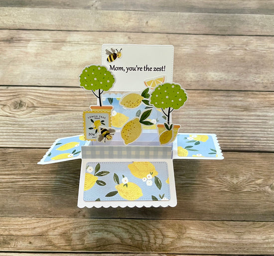 Pop-up card with lemon design and 'Mom, you're the zest!' message on a wooden surface