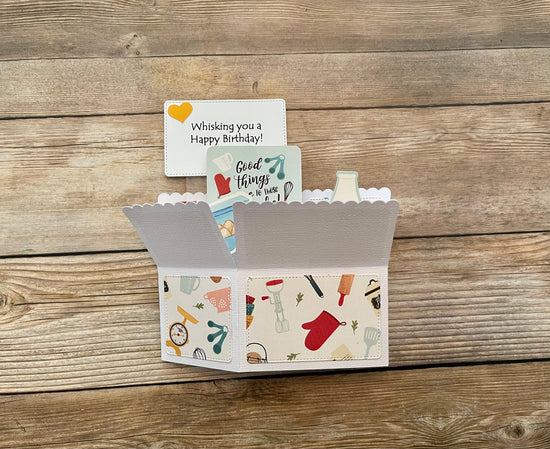 Box style pop-up card with baking theme shown folded on a wooden background
