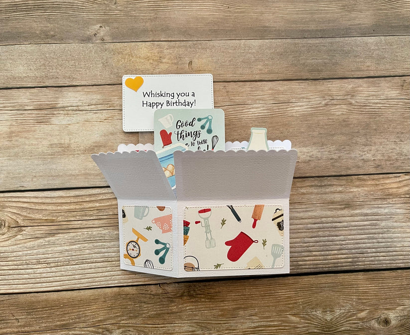 Box style pop-up card with baking theme shown folded on a wooden background