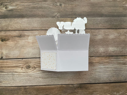 White decorative box style pop-up card folded flat with stars design on a wooden surface