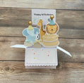 Pop-up card with animal illustrations and 'Happy 1st Birthday' text on a wooden background