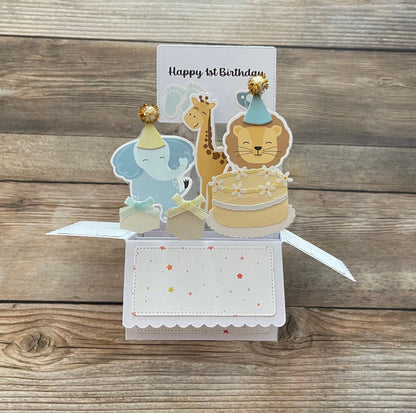 Pop-up card with animal illustrations and 'Happy 1st Birthday' text on a wooden background