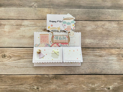 Pop-up card with cut-out elements celebrating baby's first birthday folded flat on a wooden surface