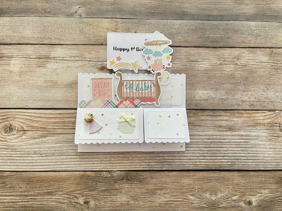 Pop-up card with cut-out elements celebrating baby's first birthday folded flat on a wooden surface