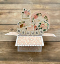 Decorative card with floral designs and 'MR & MRS' text on a wooden surface