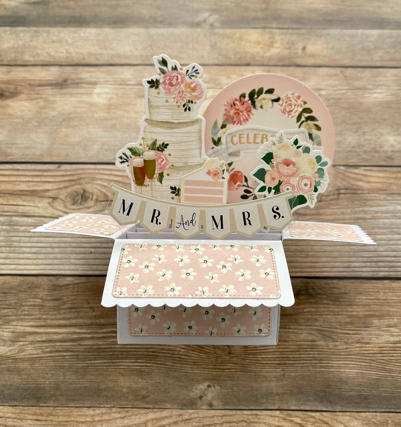 Decorative card with floral designs and 'MR & MRS' text on a wooden surface