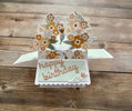 Pop-up birthday card with floral design and 'happy birthday' text on a wooden surface