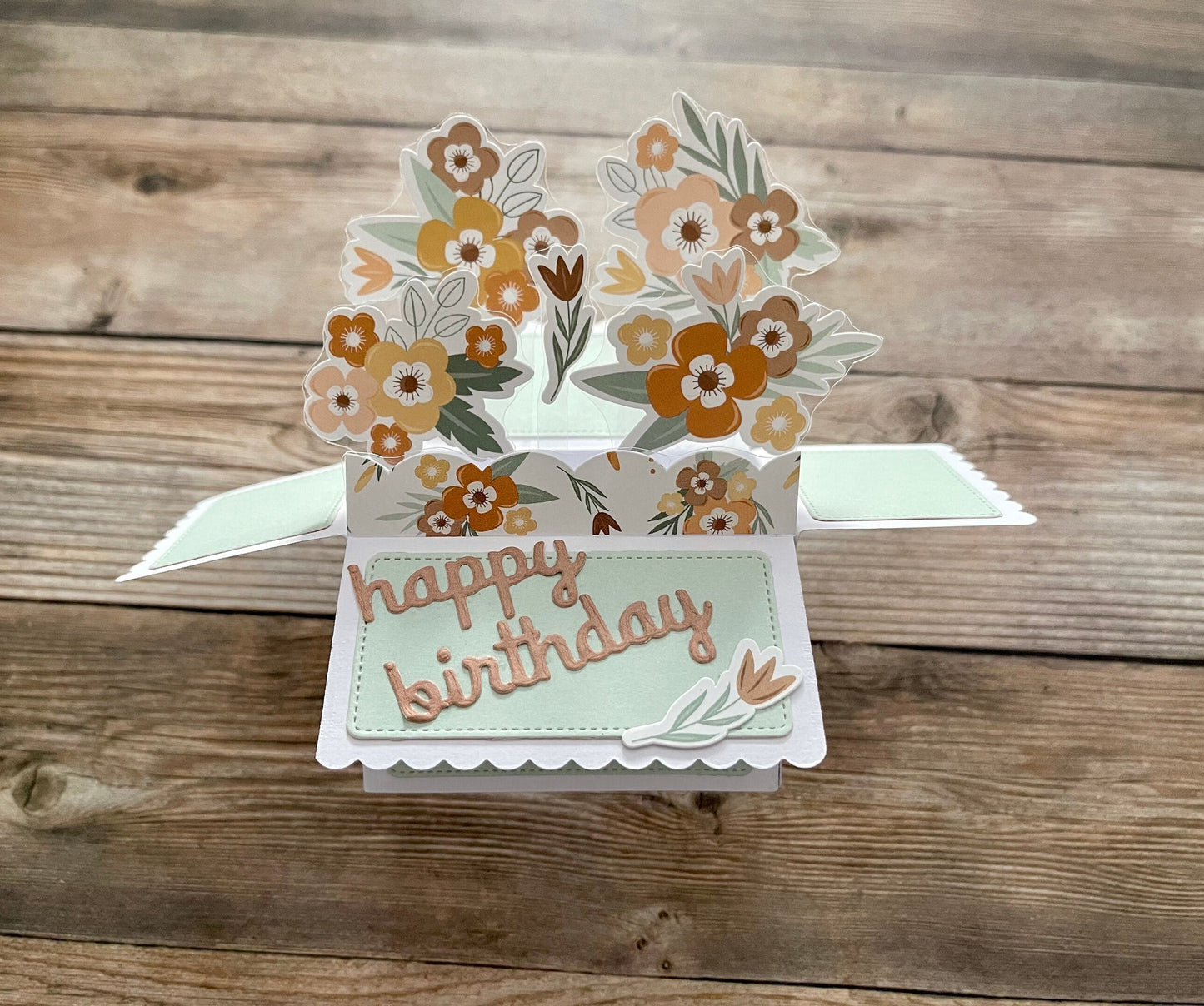 Pop-up birthday card with floral design and 'happy birthday' text on a wooden surface