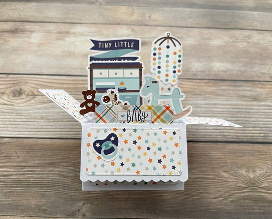 Pop-up card with baby nursery elements on a wooden surface